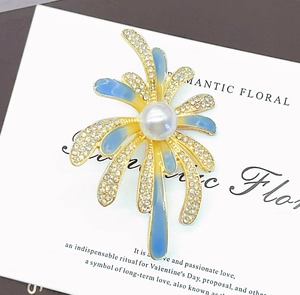 Détail macro d'une broche feu d'artifice avec pétales dorés, cristaux et perle centrale
