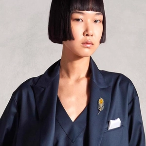 Détail de la luxueuse broche plume dorée avec gemme jaune sur un blazer bleu marine