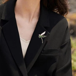 Elegante Libellen-Brosche mit grünen Edelsteinen und weißer Perle auf schwarzem Blazer