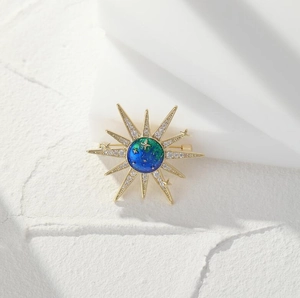 Macro view of gold sunburst brooch with blue-green enamel and sparkling crystals