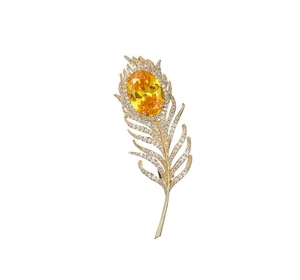 Détail d'une broche plume dorée avec une pierre jaune à facettes et des cristaux scintillants