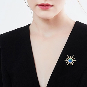 Close-up of golden sunburst star brooch with a blue-green iridescent bead on a black blazer