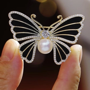 Élégante broche papillon en émail noir avec cadre doré, perle centrale et cristaux brillants