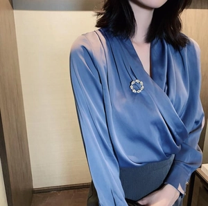 Détail de la broche perle feuille sur une élégante blouse en satin bleu col en V