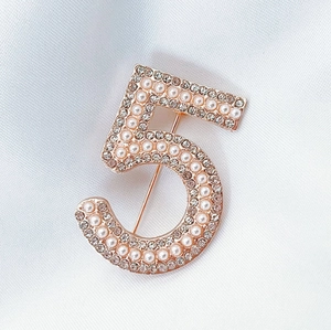 Close-up of rose gold number 5 brooch with inlaid pearls and sparkling crystals