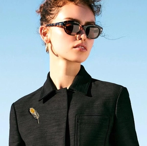 Détail d'une broche plume dorée avec gemme jaune sur une veste en tweed noir