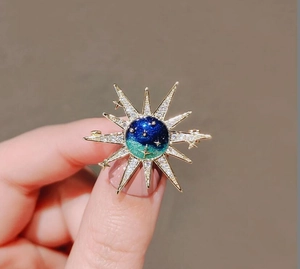 Macro view of sunburst celestial brooch featuring blue gradient and cubic zirconia