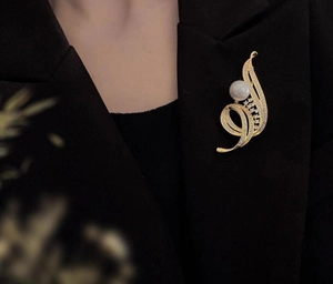 Gros plan détaillé d'une broche plume dorée avec perle sur une veste noire de tailleur