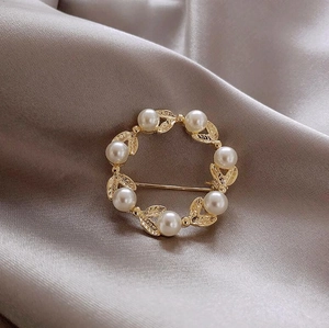 Vue détaillée de la broche couronne de feuilles dorées avec perles sur fond de tissu en soie