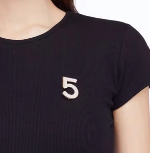 Detailed view of a number 5 pearl brooch pinned on a black ribbed knit garment
