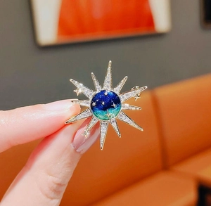 Macro shot of sunburst brooch with celestial blue gradient center and sparkling crystals