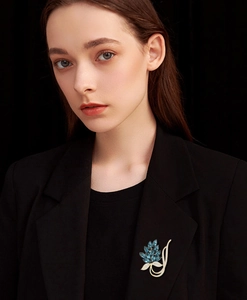 Detail showing elegant blue leaf brooch with sparkling crystals on black blazer lapel