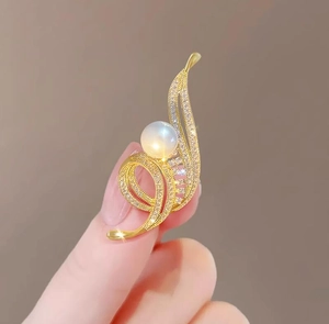 Détail d'une broche fleur dorée avec perle blanche et strass brillants tenue à la main