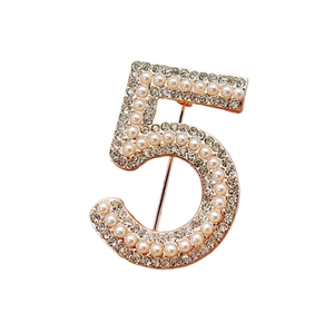 Detailed view of number 5 brooch with golden base, white pearls and sparkling rhinestones