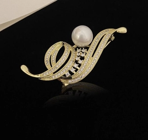 Détail d'une broche fleur dorée avec perle blanche et cristaux brillants sur fond noir