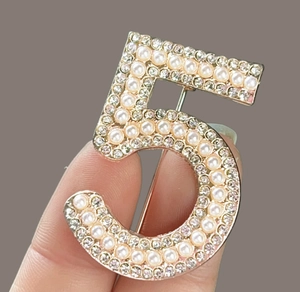 Detailed view of number 5 brooch with inlaid pearls and sparkling rhinestones