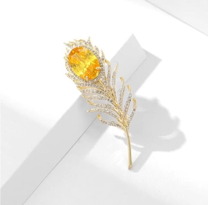 Détail de luxe d'une broche plume dorée avec pierre jaune et zircons scintillants