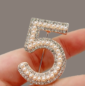Detail of elegant gold number 5 brooch with inlaid pearls and sparkling crystals