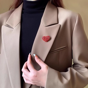 Dettaglio macro di una spilla a cuore con cristalli rossi su un blazer di classe