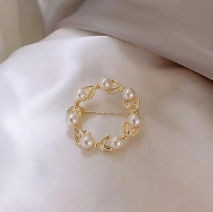 Détail d'une broche couronne dorée avec perles blanches et motif de feuilles ajourées
