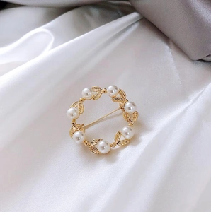 Détail d'une broche en perles dorées avec texture de feuilles sur fond en satin argenté