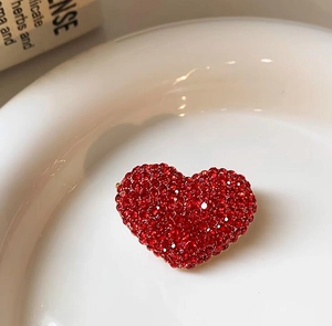 Vista macro di un'elegante spilla a cuore rossa con strass su piatto di ceramica