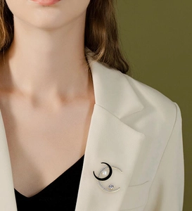 Detail of crescent moon brooch with black enamel and pearls on a white blazer lapel