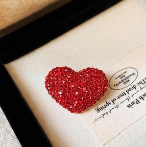 Dettaglio macro di spilla a cuore con strass rossi su elegante espositore per gioielli