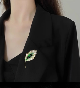 Elegant gold leaf brooch with pear-shaped green stone and pavé crystals on a black blazer