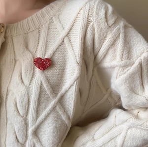 Dettaglio ravvicinato di una spilla a cuore con cristalli rossi su un maglione di maglia crema