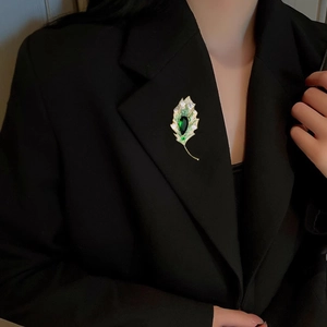 Close-up of elegant leaf brooch with emerald gemstone pinned on a black suit blazer