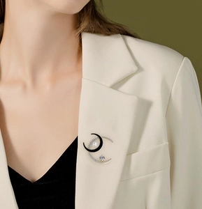 Close-up of sparkling moon brooch with crystals and pearl on a white suit lapel
