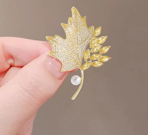 Detailed close-up of maple leaf brooch with yellow crystals and elegant white pearl