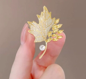 Detail of yellow maple leaf brooch with sparkling crystals and a white pearl accent