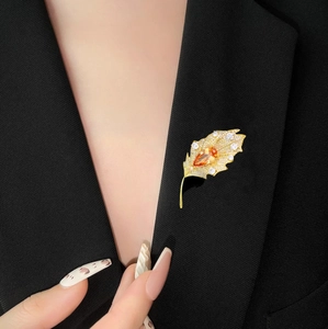 Detail of golden leaf brooch with white crystals and orange gemstone on black suit
