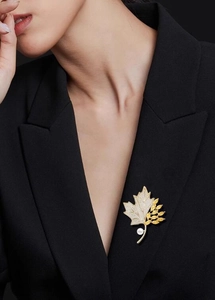 Detailed view of yellow crystal maple leaf brooch with white pearl on black suit jacket