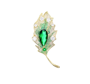 Close-up of golden leaf brooch with pear-cut green gemstone and sparkling zircons