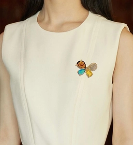 Detail einer eleganten Schmetterlingsbrosche mit farbigen Tropfensteinen auf hellem Kleid