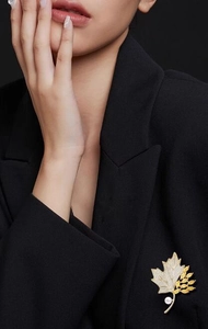 Detail of maple leaf brooch with yellow stones and pearl on black blazer lapel