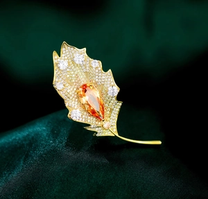 Macro detail of leaf brooch with orange teardrop stone and white zircon pave setting