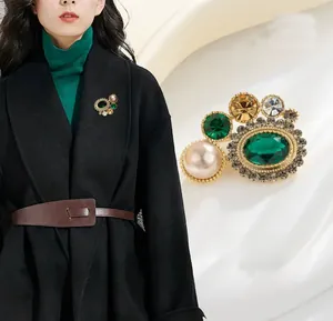 Gros plan détaillé d'une broche vintage aux pierres vertes et une grande perle rose