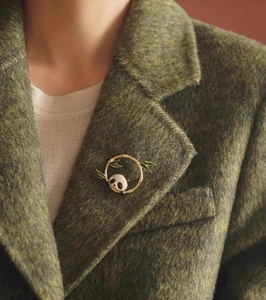 Dettaglio della spilla con panda e bambù sul bavero di un cappotto di tweed verde