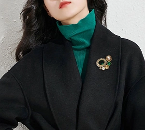 Broche géométrique vintage avec émeraudes et perles sur un manteau noir élégant