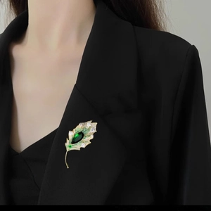 Elegant gold leaf brooch with green teardrop crystal pinned on black suit jacket
