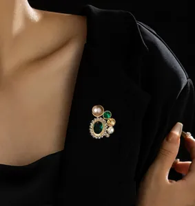 Détail d'une broche vintage dorée avec pierre vert émeraude et perle sur un blazer