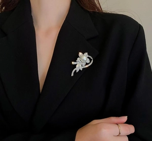 Close-up of a silver flower brooch with a large pearl center and rhinestones on a black blazer