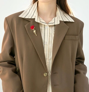 Elegant red rose brooch on brown blazer lapel featuring gold metal stem details