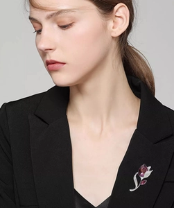 Detailansicht einer eleganten lila Blumenbrosche mit Glitzersteinen auf schwarzem Blazer