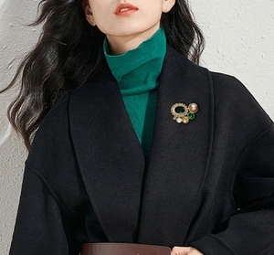 Gros plan d'une broche vintage en émeraude avec perles et cristaux sur un manteau