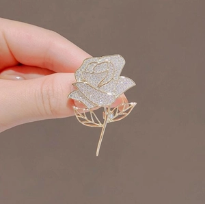 Elegant gold rose brooch with sparkling zircon crystals held against a brown background